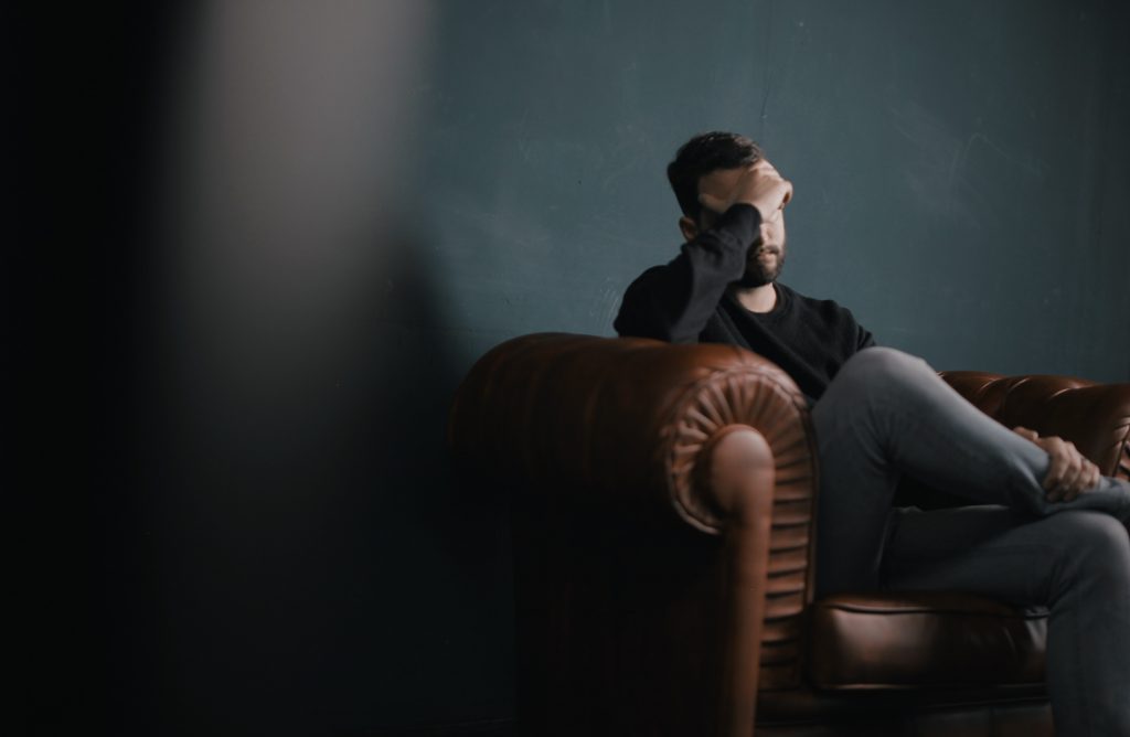 Man sitting on sofa with head in hand looking concerned