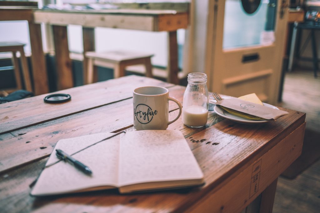 Coffee shop table with an open thoughts journal with cup and milk